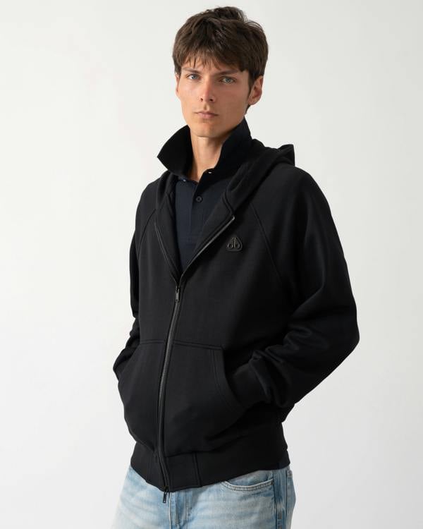 a model wearing a Moose Knuckles Mens Yul Zip Up Hoodie in Black 292