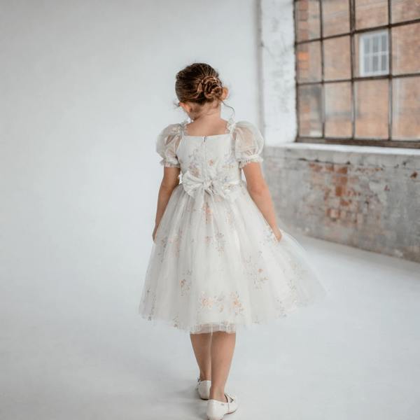 Young girl in a white lace dress standing in a room with brick walls.
