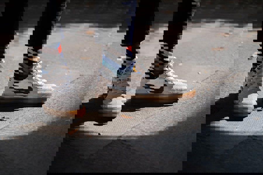 White sneakers with black Nike logo combined with bold stripe socks worn on a sidewalk