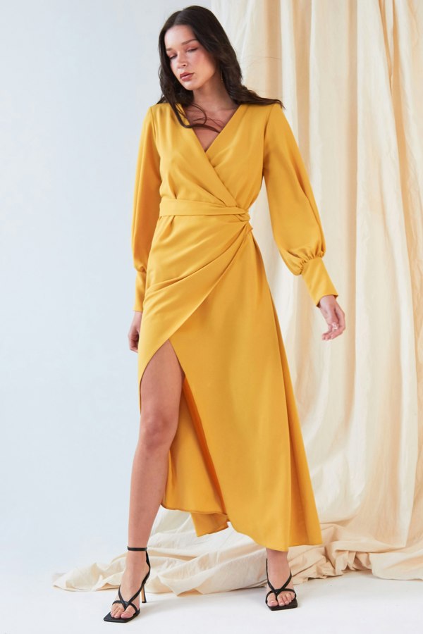 The model is wearing a Sarvin Mustard Wrap Dress with a slit.