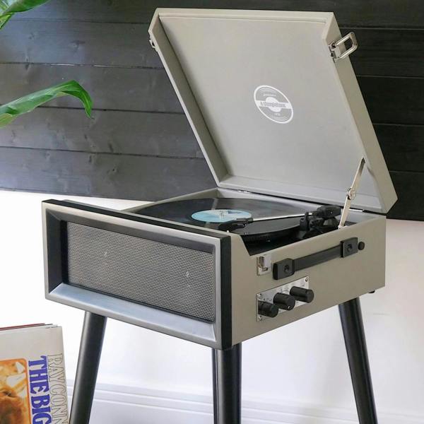 A retro style grey vinyl record player on black legs with an open lid, playing a vinyl record in a stylish living space.