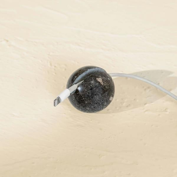 Black marble cable tidy with a white cable on a beige background