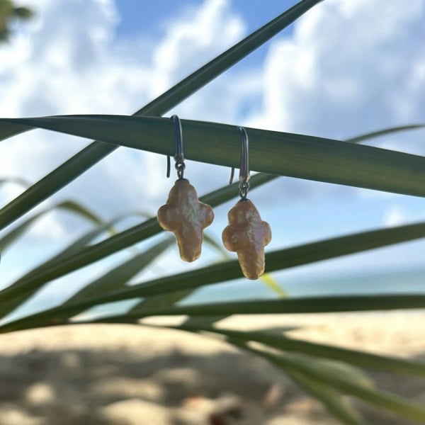 Cross-shaped pearl earrings by LENAE, handcrafted in London in sterling silver. Shown on a pal leaf.