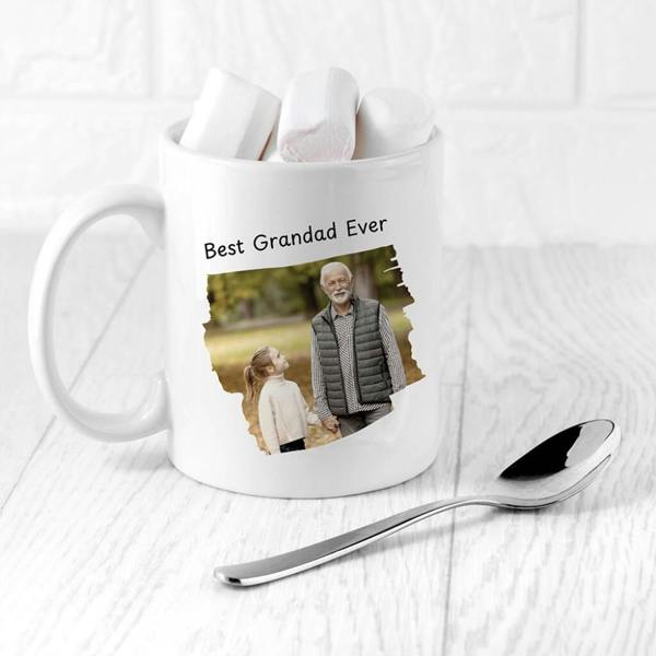 A white ceramic mug from Abode Home & Gifts printed with 'Best Grandad Ever' text and a custom photo of a grandfather and granddaughter holding hands outside.