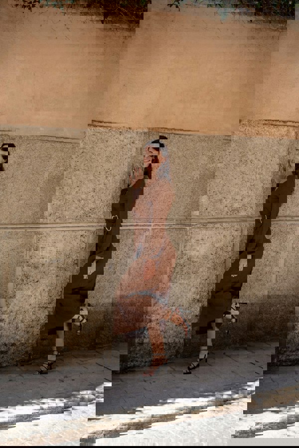 Woman in a brown dress standing against a textured wall.