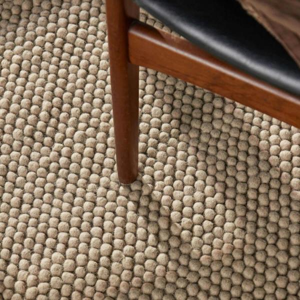 Close-up of a textured beige carpet with a wooden chair leg.