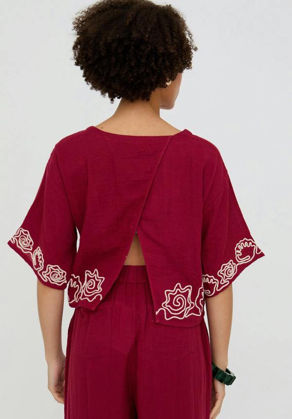 Person wearing a burgundy outfit with floral embroidery on a plain background
