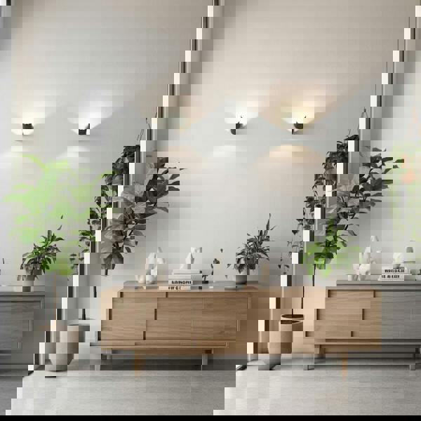 Black indoor wall uplighter on a grey wall with a side board and plants below the light