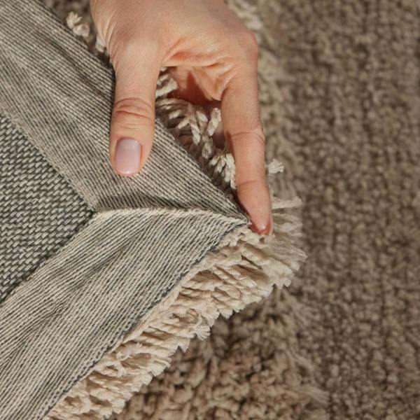 Hand holding the edge of a textured rug against a matching carpet