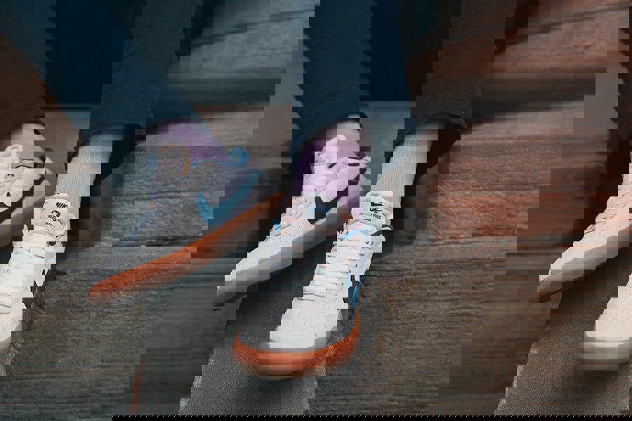 White sneakers with purple socks worn on a person sitting on steps.