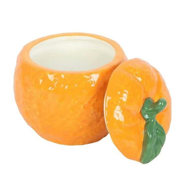 Orange-shaped candle jar with lit wick and matching orange side jar with green leaf