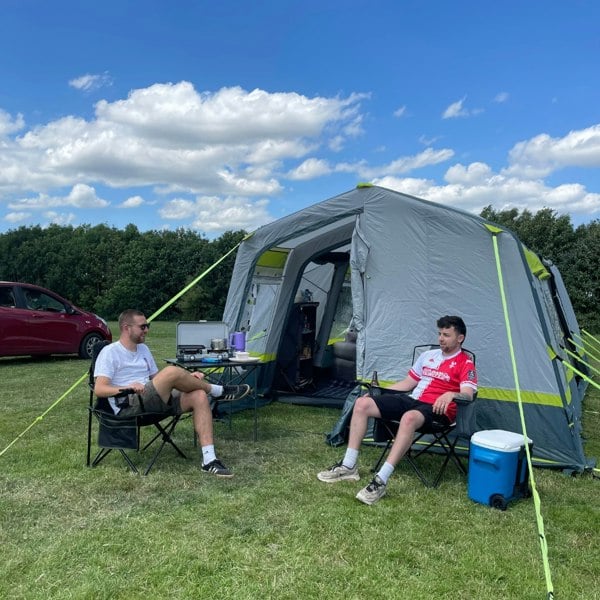 Two males sat relaxing outside of the OLPRO Home 5 Berth Inflatable Family Tent on a campsite.