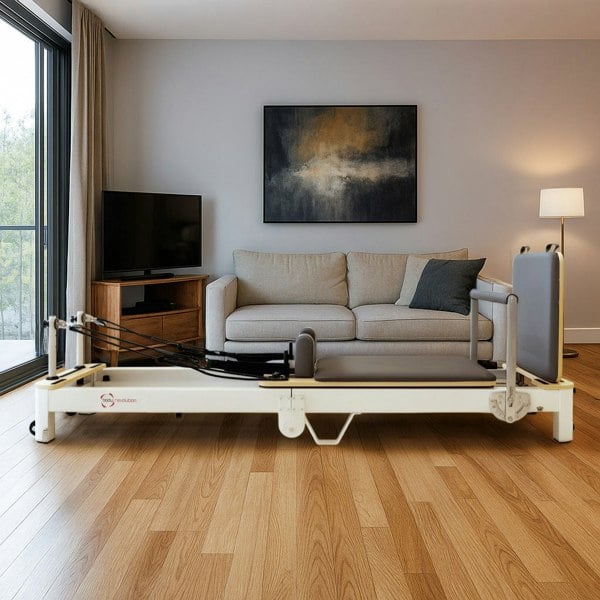 Aluminium Pilates reformer machine in a modern living room, featuring a sleek design, padded surface, and adjustable straps on a wooden floor