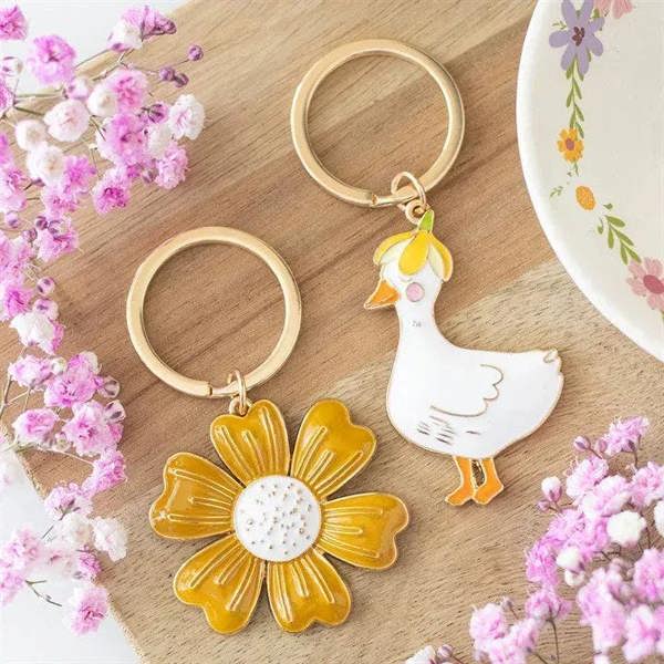 Two keyrings: gold-tone ring, white duck enamel charm, and yellow flower charm