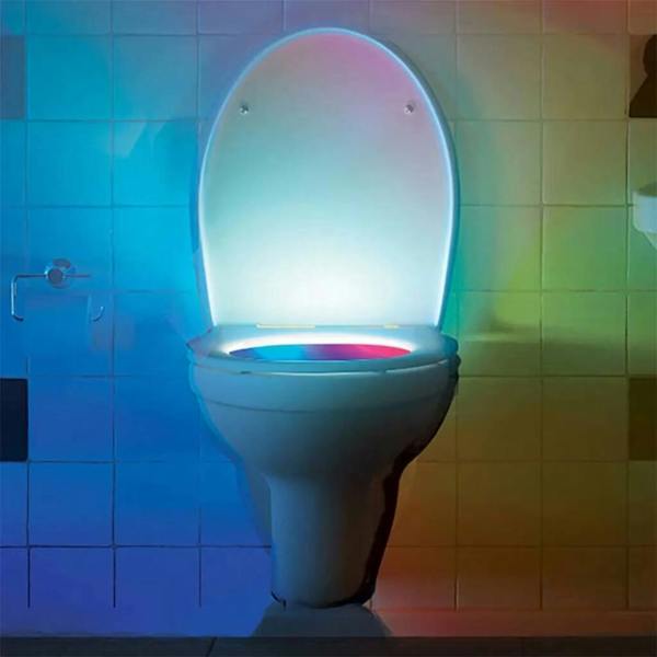 A white toilet in a tiled bathroom illuminated in the dark by a multi-coloured motion-activated night light glowing with blue, pink, and yellow hues.