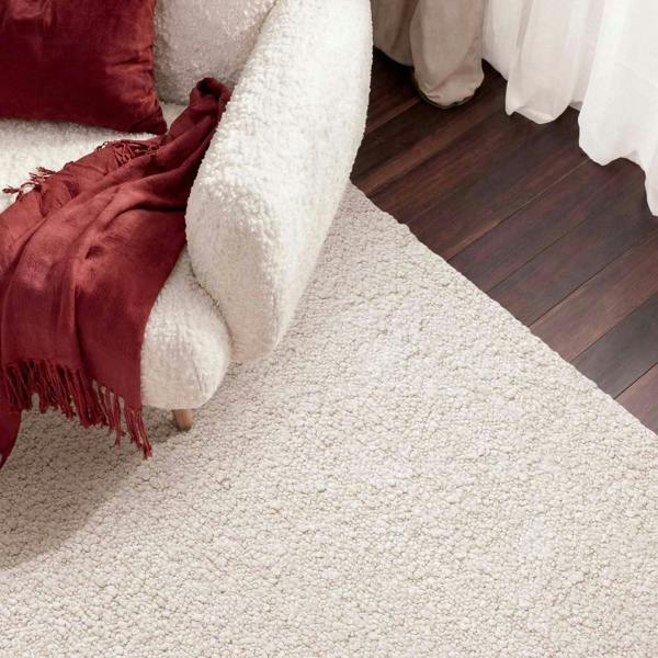 Close-up of a textured beige carpet with a white sofa and red cushions.