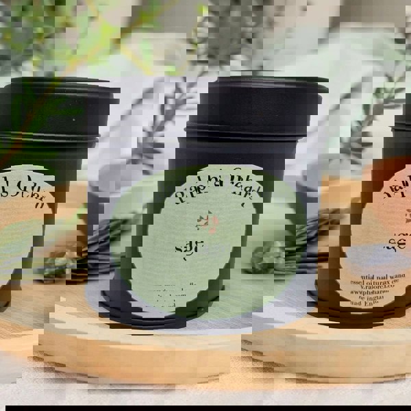 Candle in a black tin labeled 'Ralph's Orchard Sage' on a wooden surface with plants in the background.