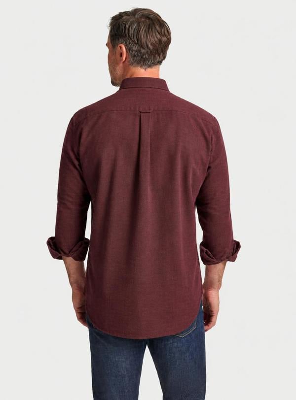 A man viewed from the back wearing a maroon long-sleeve button-down shirt with rolled-up sleeves and blue jeans, set against a plain light gray background.
