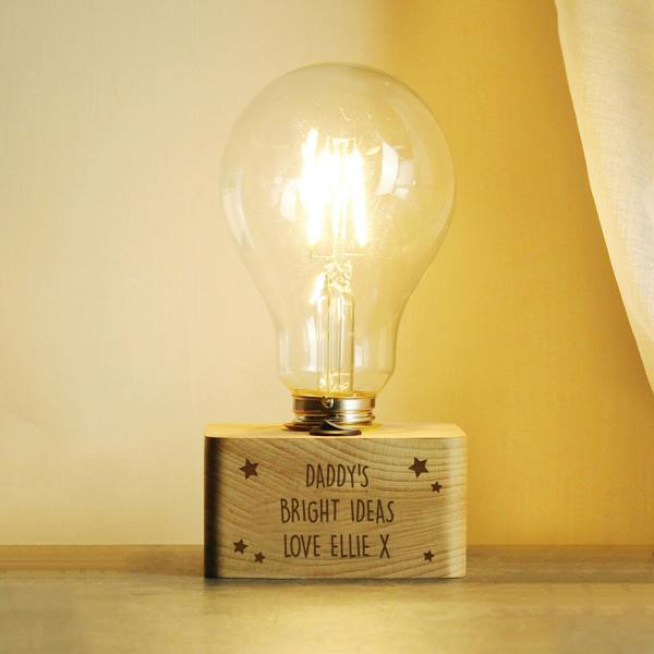 A personalised stars LED bulb table lamp by Abode Home & Gifts with a solid wooden base engraved with "DADDY'S BRIGHT IDEAS LOVE ELLIE X" lit up against a soft grey background.