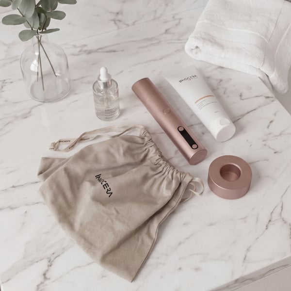 Flat lay of the Innocera Max™ skincare system showing the device, charging dock, Innocera Conductor Gel, Radiance Anti-Ageing Serum, USB-C charging cable and branded travel pouch.