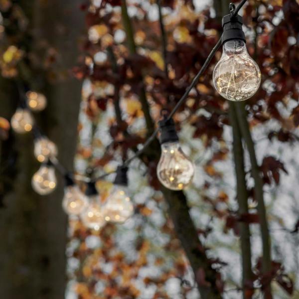 Classic outdoor festoon lights with 20 bulbs on a black cable, draped through autumn trees to create a warm festival glow.