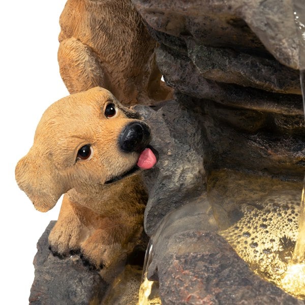 Realistic golden retriever puppy sculpture beside a cascading water feature, featuring textured rocks and gentle water flow