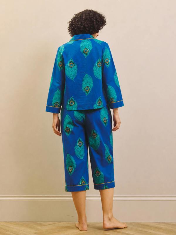 Model wears a pair of navy peacock print capri pyjamas against a beige wall