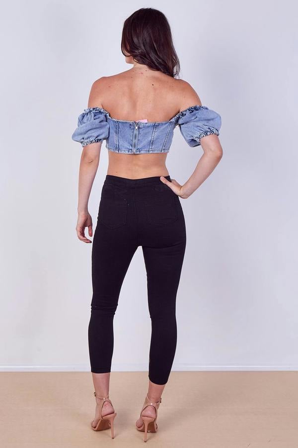 Woman wearing a denim off-shoulder top against a plain background