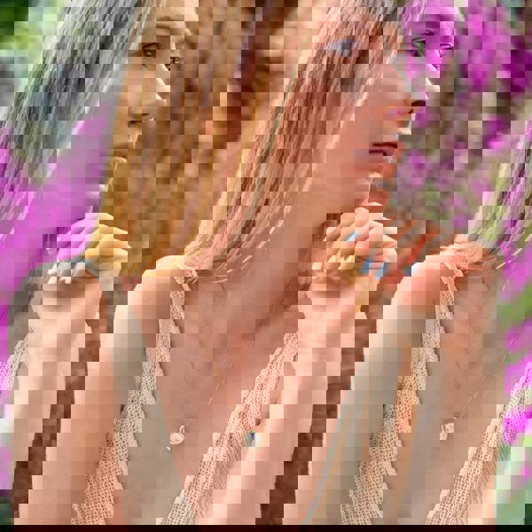 Bloomtine-Loves-Frequency-necklace-lifestyle. A professional-lifestyle-shot of a woman-wearing-the-signature-gold-heartbeat-pendant-necklace against a backdrop-of-soft-purple-flowers. This-18kt-gold-vermeil-jewellery features a unique-heartbeat-frequency-design, symbolizing-connection-and-love. The-natural-lighting highlights the-polished-finish, while the-floral-setting-emphasizes the-romantic-botanical-aesthetic of the Bloomtine-brand. An-ideal-meaningful-gift for anniversaries-or-special-occasions, show