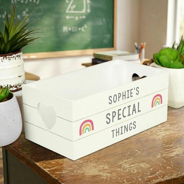 Personalised white wooden storage crate with rainbow details and heart cutout handles on a rustic table.