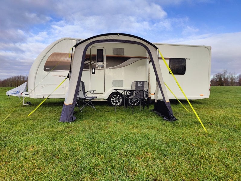 An image of the View Lite 260 Caravan Awning from OLPRO in a field attached to a caravan with some camping furniture inside.