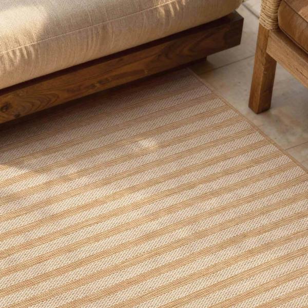Striped beige and white rug on a wooden floor with a part of a beige sofa visible.