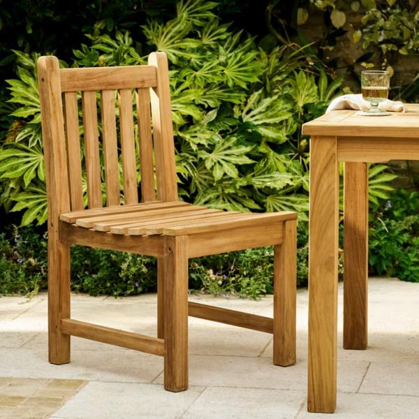 Front-angled view of a solid teak garden armchair with a multi-slatted back on a stone patio.