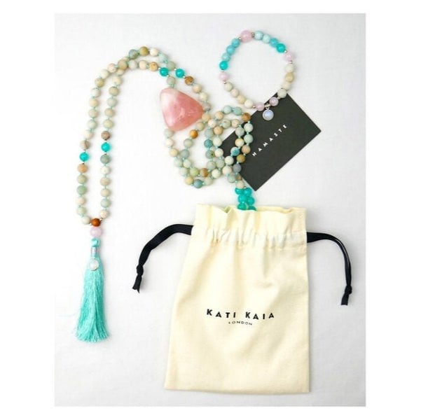 Kati Kaia Crystal Mala Necklace with pastel beads and turquoise tassel alongside branded drawstring pouch