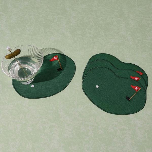 A set of four green linen cocktail napkins shaped like golf putting greens with embroidered white balls and red 19 flags, featuring a crystal cocktail glass sitting on one napkin.