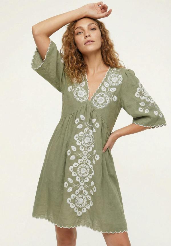 Woman wearing a green dress with white embroidery on a light background