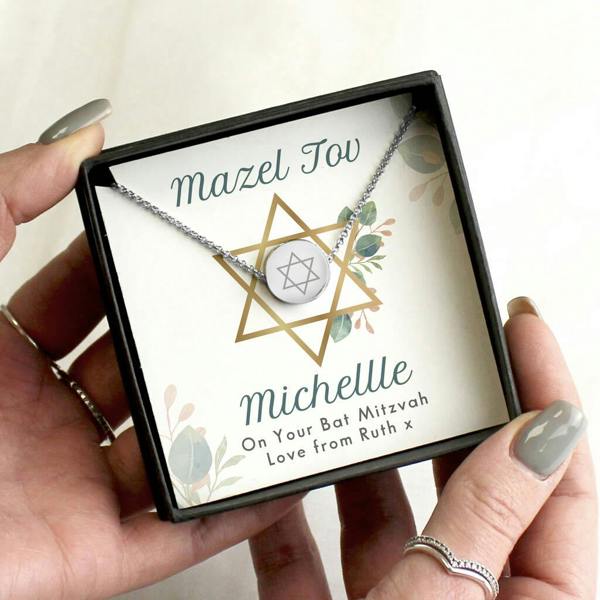 A silver-tone round pendant necklace engraved with a Star of David, presented in a black gift box reading 'Mazel Tov Michelle'.