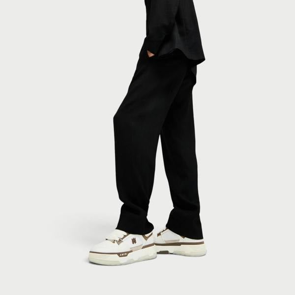 Supplied Fashion AMIRI MA-1 white and brown leather sneakers worn with black trousers in a side profile view