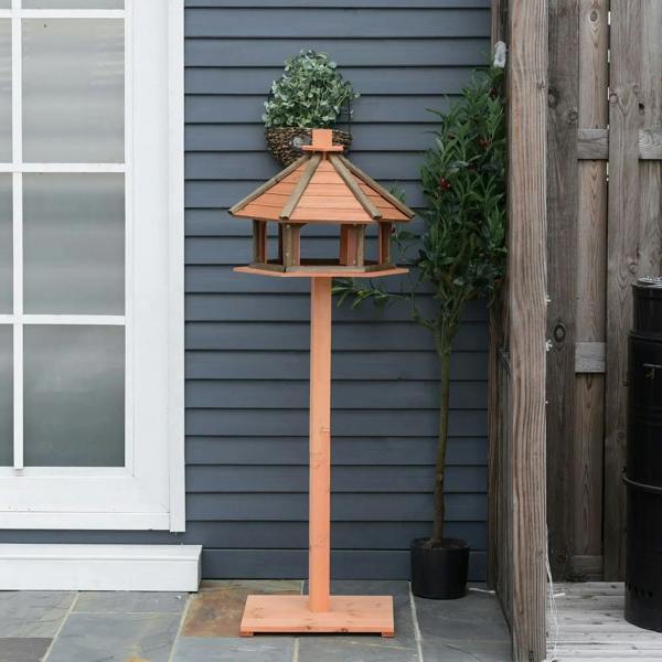 Brown wooden bird feeder with slanted hexagonal roof and open tray on post