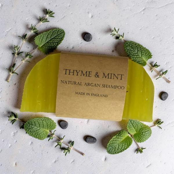 Green bar of soap with a 'Thyme & Mint' label on a light background with herbs.