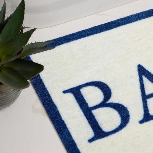 White bath mat with blue border and 'BA' text, next to a potted plant.