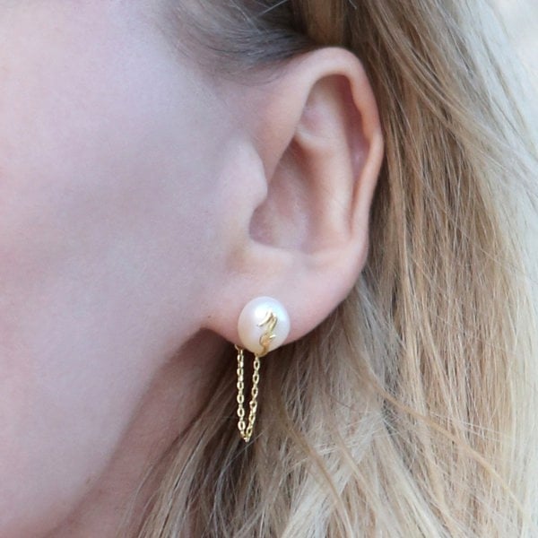 An ear with a pearl stud earring that has chain and is embellished.