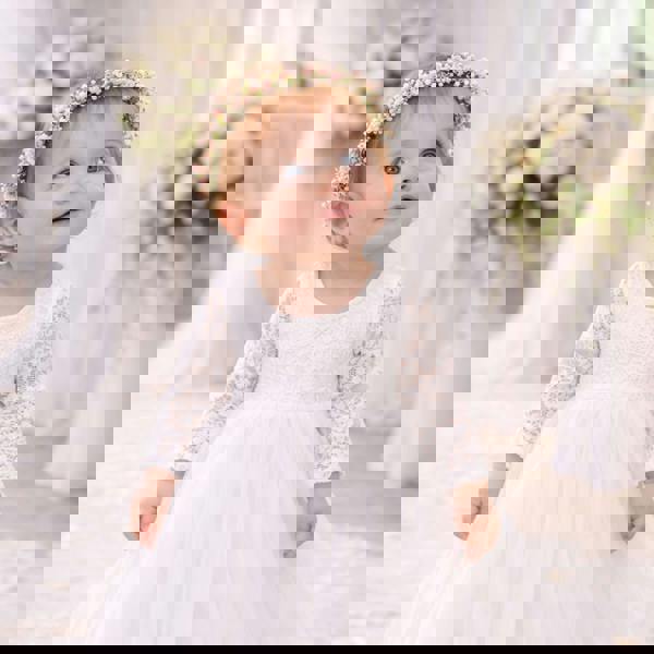 Baby in a white dress with floral headband in a softly blurred indoor setting