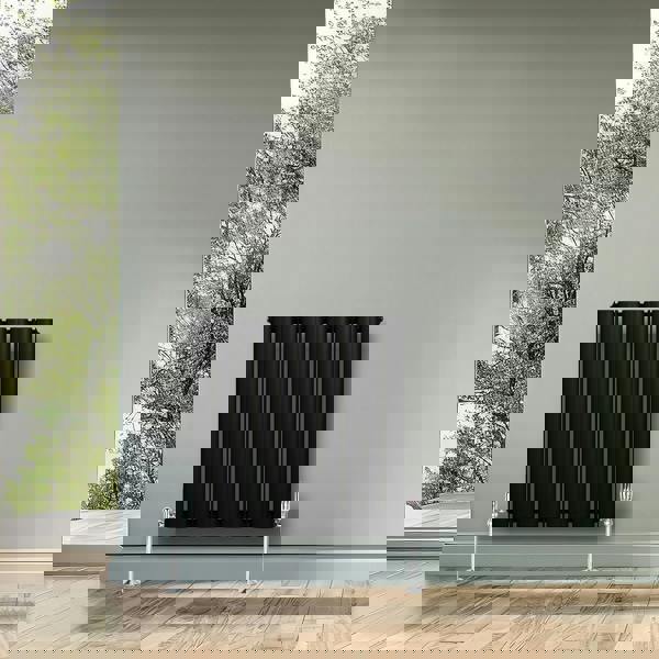 Sleek black oval single column radiator mounted on a light gray wall, complementing a modern interior with wooden flooring