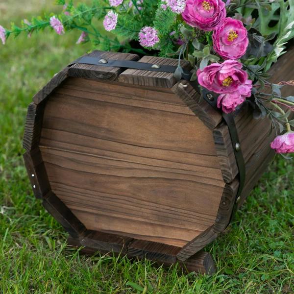 Angled view of dark brown wooden planter box end with metal straps and pink flowers