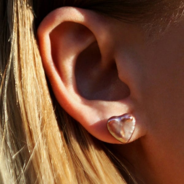 Close up of an ear with pink heart-shaped pearl studs.