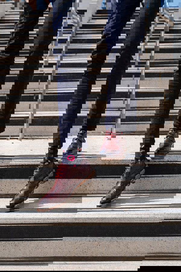 Person wearing navy chinos with navy pink socks and brown shoes on a set of concrete stairs.