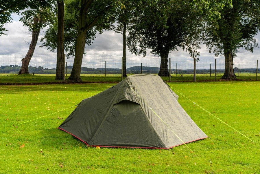 The OLPRO Hawford Lightweight 2 Person Tent pitched in a field with a treeline in the background, the doors are closed and the vents are open.