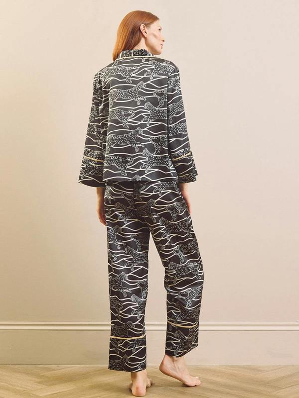A person wearing a matching pyjama set with a black base and white abstract animal print, shown from the chest down against a plain beige studio background.