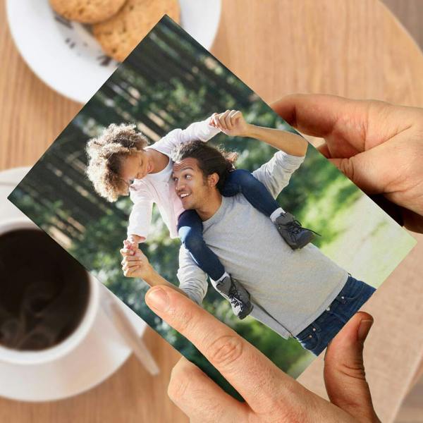 A person’s hands holding a high-quality portrait Father’s Day card featuring a custom photo of a smiling father giving his young daughter a shoulder carry outdoors.